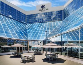 Open-air terrace with patio tables, umbrellas, and glass hotel façade reflecting blue skies.