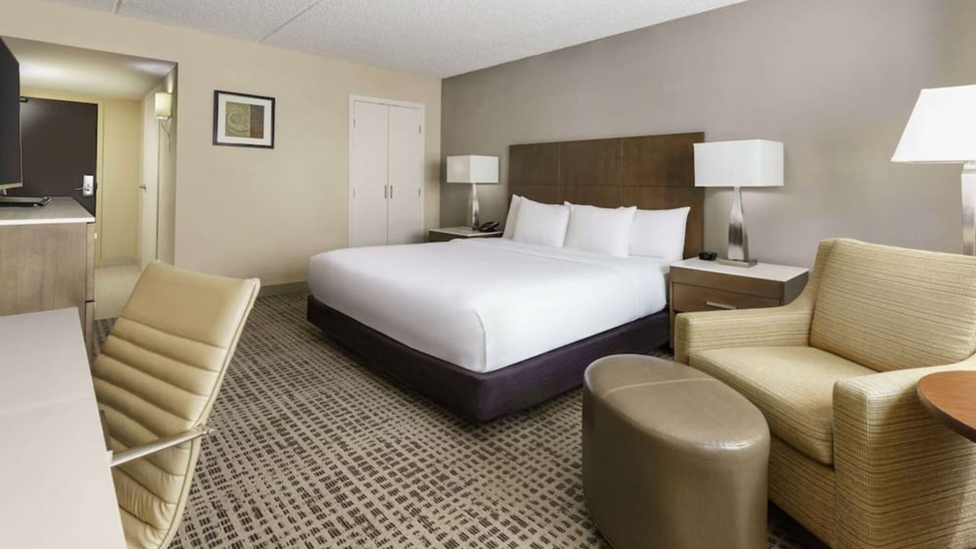 Contemporary king guest room featuring seating area, ottoman, work desk, and neutral-toned décor.
