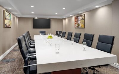 Private meeting room with long conference table, leather executive chairs, and wall-mounted display.