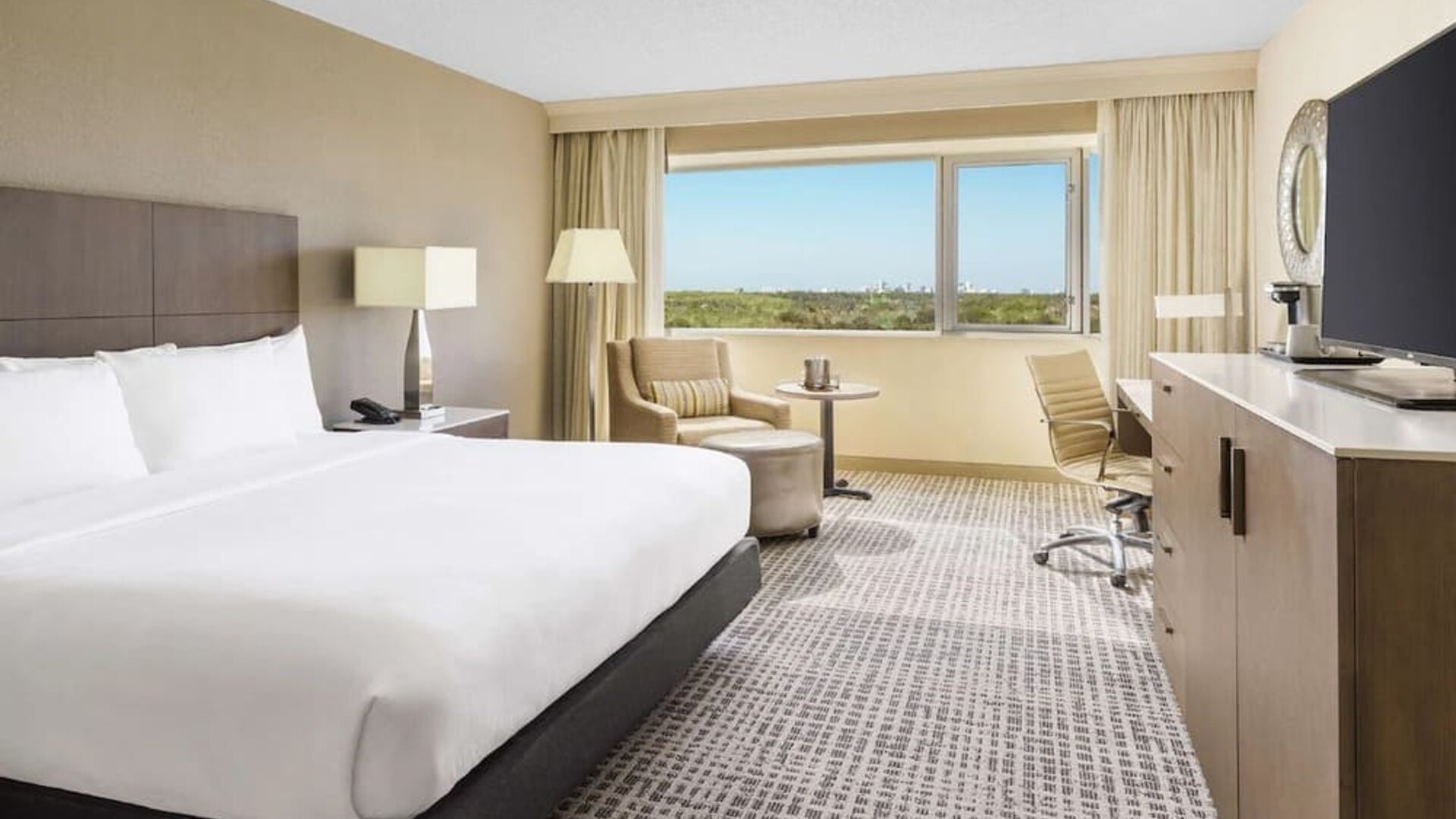 King suite with large bed, sitting area, work desk, and expansive window overlooking greenery.