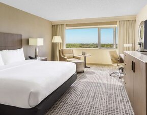 King suite with large bed, sitting area, work desk, and expansive window overlooking greenery.