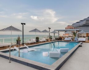 Poolside loungers beneath striped umbrellas overlooking the ocean during a soft coastal sunset.
