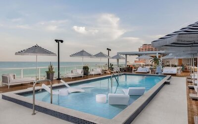 Poolside loungers beneath striped umbrellas overlooking the ocean during a soft coastal sunset.