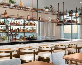Elegant ocean-view bar with marble countertop, cushioned seating, hanging shelves, and extensive liquor display.