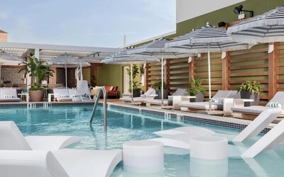 Rooftop pool deck with in-water loungers, striped umbrellas, ocean views, and comfortable relaxation areas.