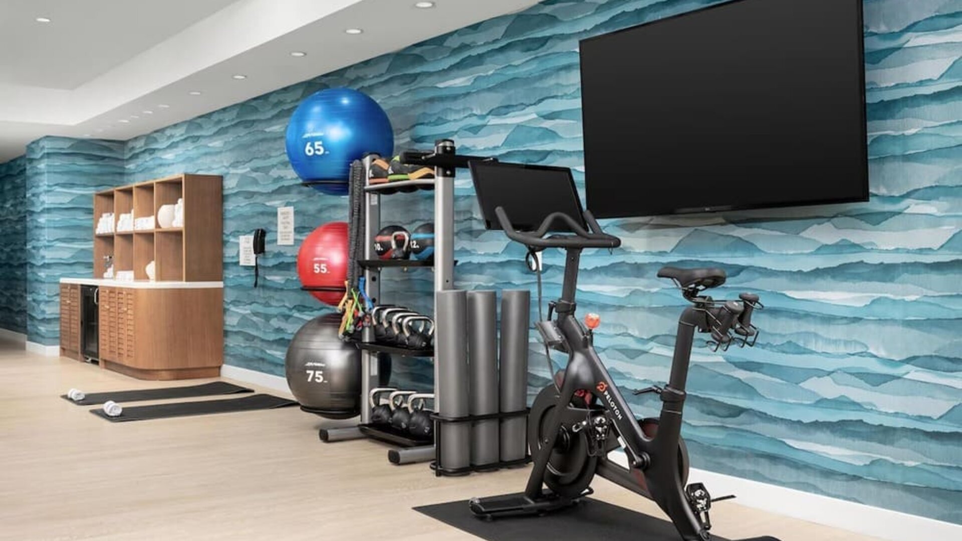Modern fitness center with stationary bike, free weights, exercise balls, yoga mats, and large wall-mounted TV.