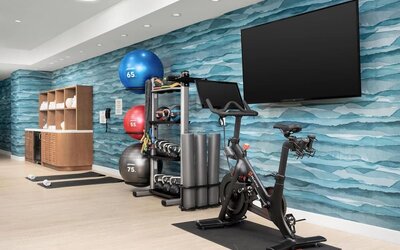 Modern fitness center with stationary bike, free weights, exercise balls, yoga mats, and large wall-mounted TV.