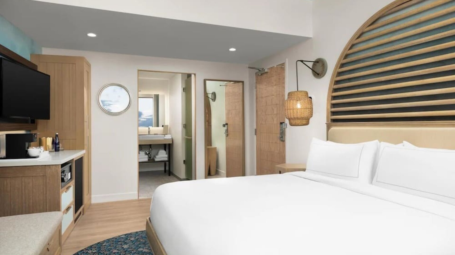 Bright guest room with king bed, wood accents, wall-mounted TV, and open vanity area leading to bathroom.