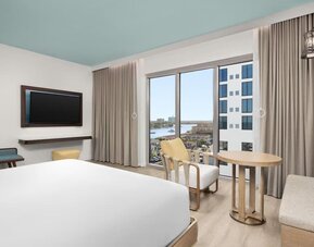 Bright king room with floor-to-ceiling windows, sitting area, round table, and views of the waterfront.