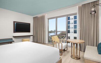 Bright king room with floor-to-ceiling windows, sitting area, round table, and views of the waterfront.