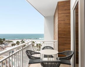 Balcony with round table and four woven chairs overlooking white-sand beach, palm trees, and turquoise ocean.