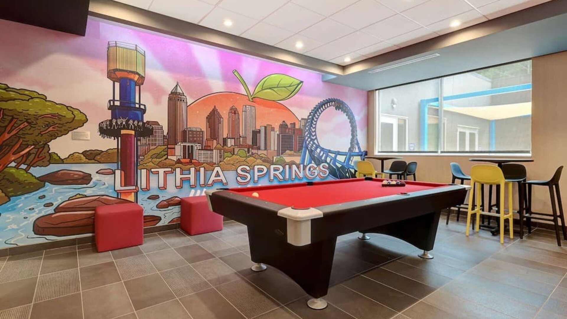 Game room with pool table, colorful Lithia Springs mural, and casual lounge seating at Tru By Hilton Lithia Springs.