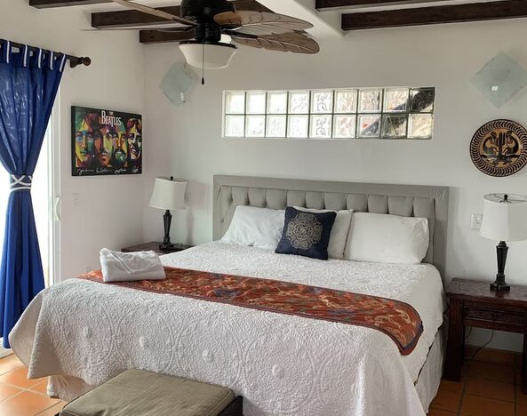 Bright king bedroom with elegant furnishings, exposed wooden beams, and adjoining lounge area at Casa Playa Baja Resort.