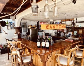 Rustic cantina-style bar with wooden seating, wine display, and beverage service at Casa Playa Baja Resort.