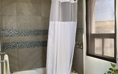 Modern bathroom featuring a bathtub with shower, tiled walls, vanity, and natural light at Casa Playa Baja Resort.