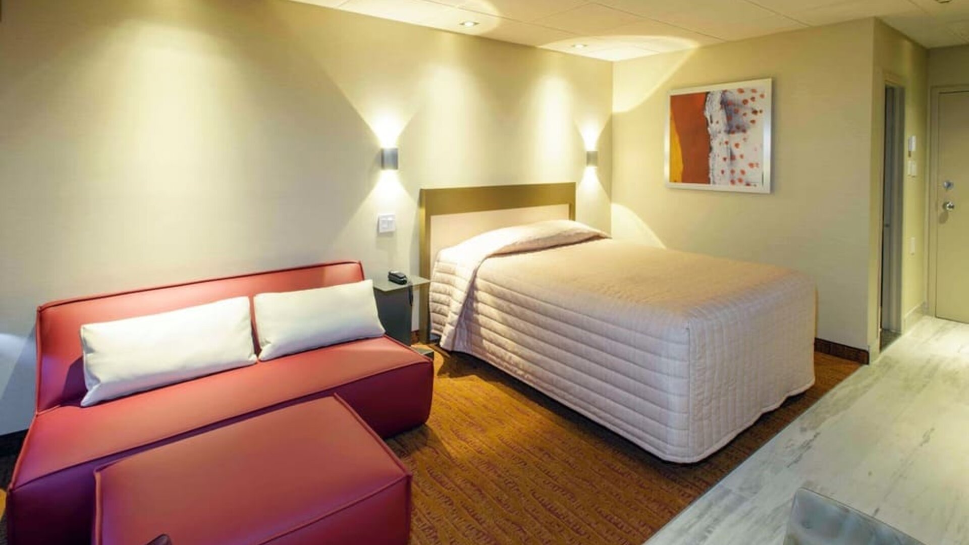 Cozy guest room with queen-size bed, lounge seating and warm contemporary décor at Le Chabrol Hotel Et Suites.