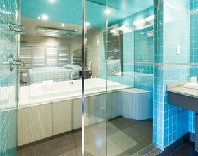 Modern bathroom with glass-enclosed bathtub, turquoise tile accents and vanity at Le Chabrol Hotel Et Suites.