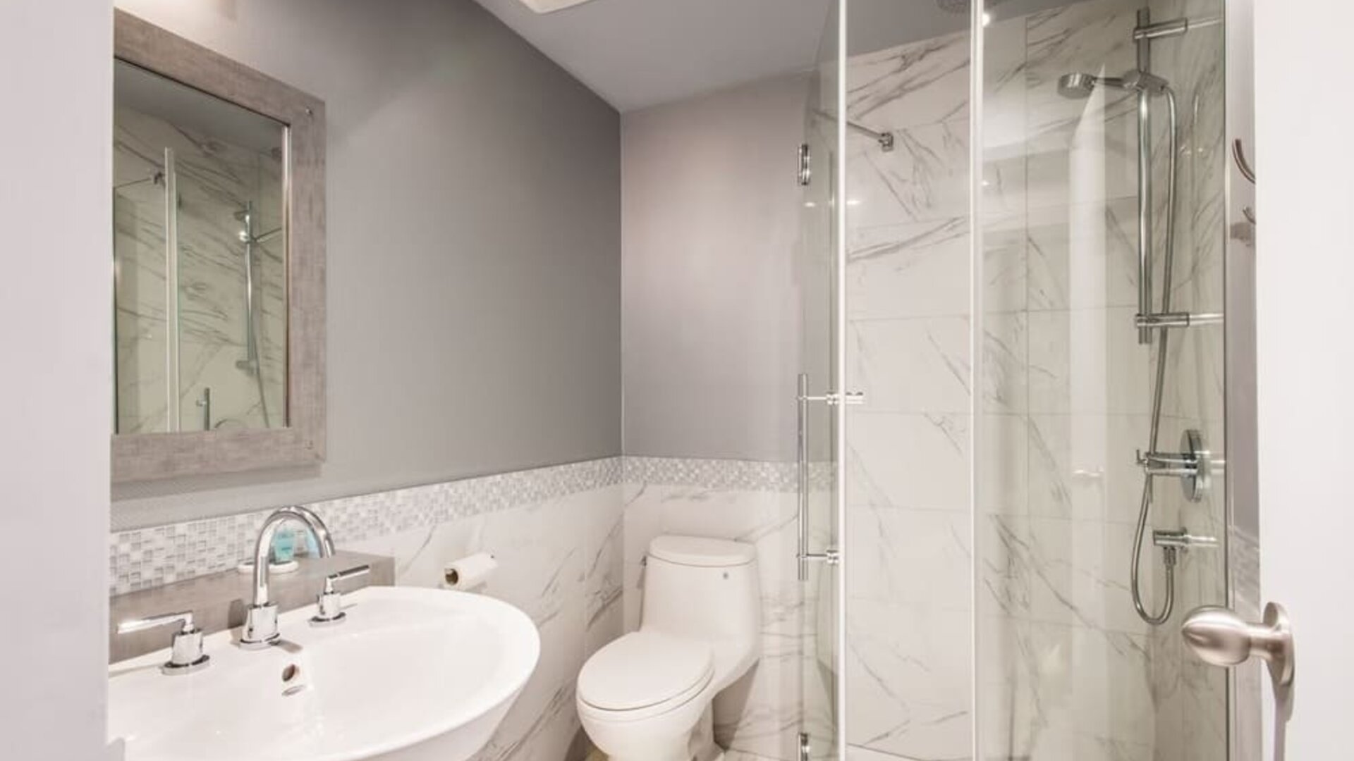 Modern bathroom with walk-in rainfall shower, marble-effect walls and elegant finishes at Le Chabrol Hotel Et Suites.