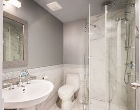 Modern bathroom with walk-in rainfall shower, marble-effect walls and elegant finishes at Le Chabrol Hotel Et Suites.