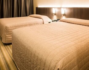 Twin guest room featuring two double beds, contemporary furnishings and warm lighting at Le Chabrol Hotel Et Suites.