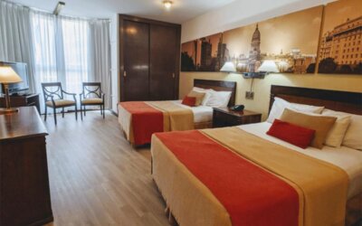 Spacious guest room at HR Plaza Luxor featuring two double beds, hardwood furnishings, city-themed artwork, and ample natural light from large windows.
