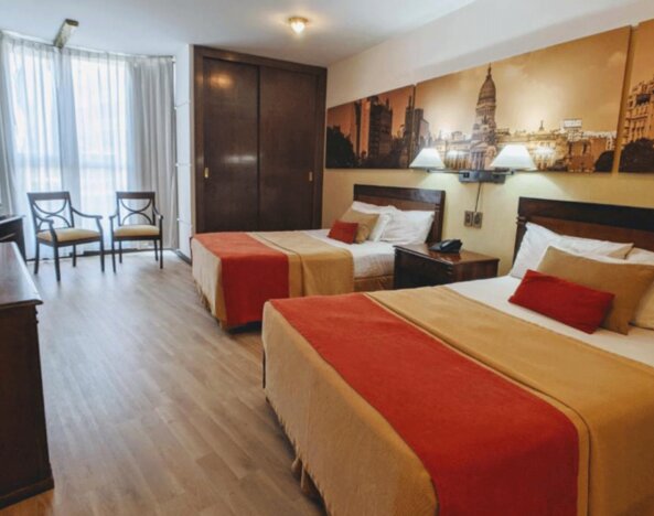 Spacious guest room at HR Plaza Luxor featuring two double beds, hardwood furnishings, city-themed artwork, and ample natural light from large windows.
