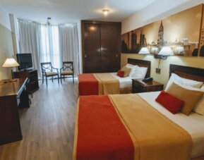 Alternative view of a guest room with two double beds, work area, flat-screen television, and warm décor designed for a comfortable stay in Buenos Aires at HR Plaza Luxor.