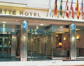 Exterior entrance of the hotel featuring an international flag display, modern glass frontage, and a prime central location at Hotel Lafayette.