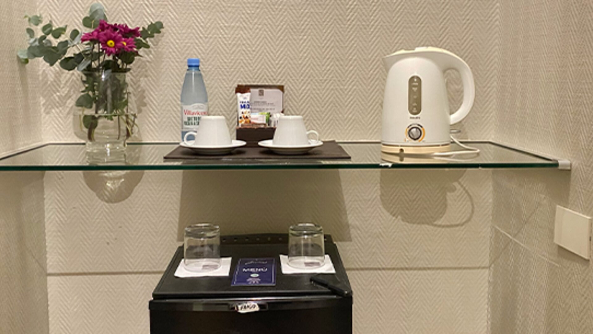 In-room refreshment station featuring complimentary bottled water, tea and coffee facilities, glassware, and a compact minibar for guest convenience at Hotel Lafayette.