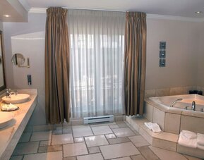 Luxury bathroom featuring a soaking tub, double vanity and spacious layout at Hotel Brossard.