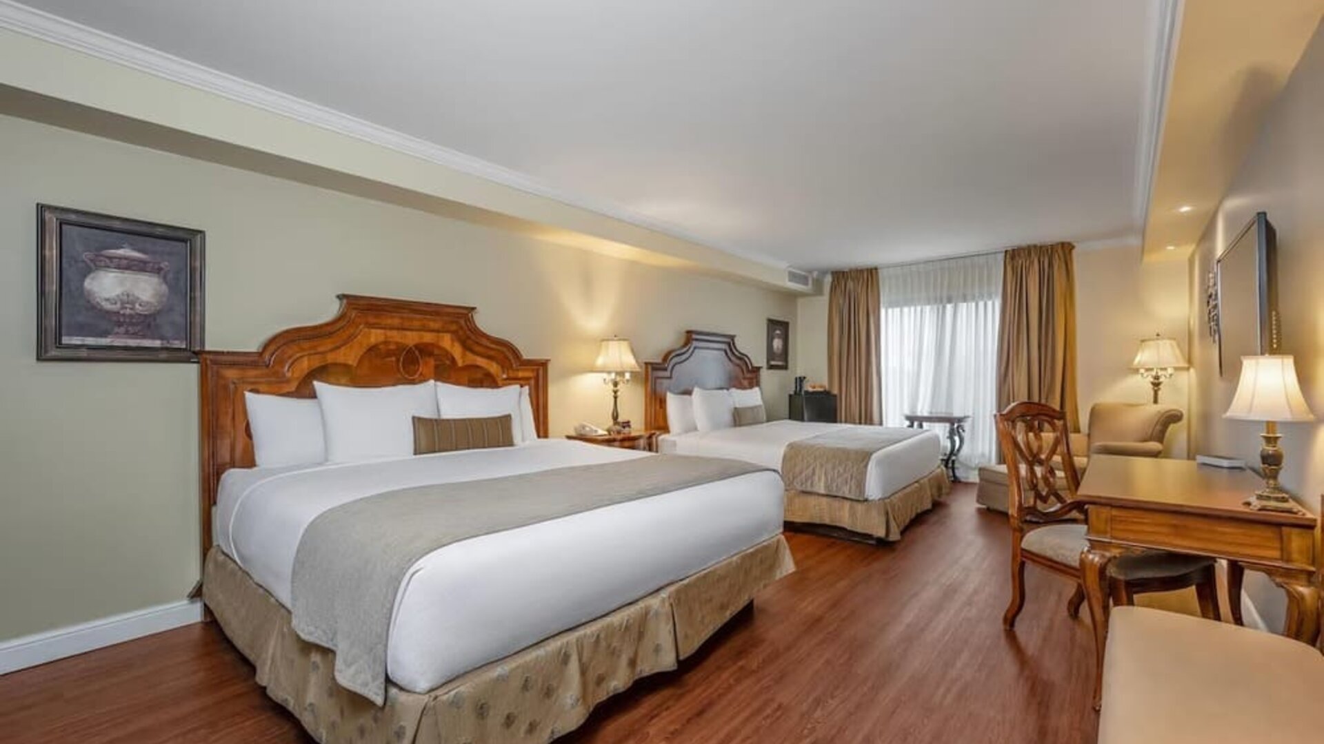 Spacious guest room with two queen beds, work desk and comfortable seating at Hotel Brossard.