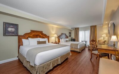 Spacious guest room with two queen beds, work desk and comfortable seating at Hotel Brossard.