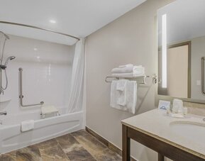 Accessible guest bathroom with bathtub, grab bars, shower seat and illuminated vanity at Days Inn & Suites By Wyndham Lindsay.