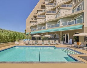 Outdoor swimming pool surrounded by lounge chairs, shaded seating, and relaxing spaces to enjoy the California sunshine at Hyatt Centric Delfina Santa Monica.