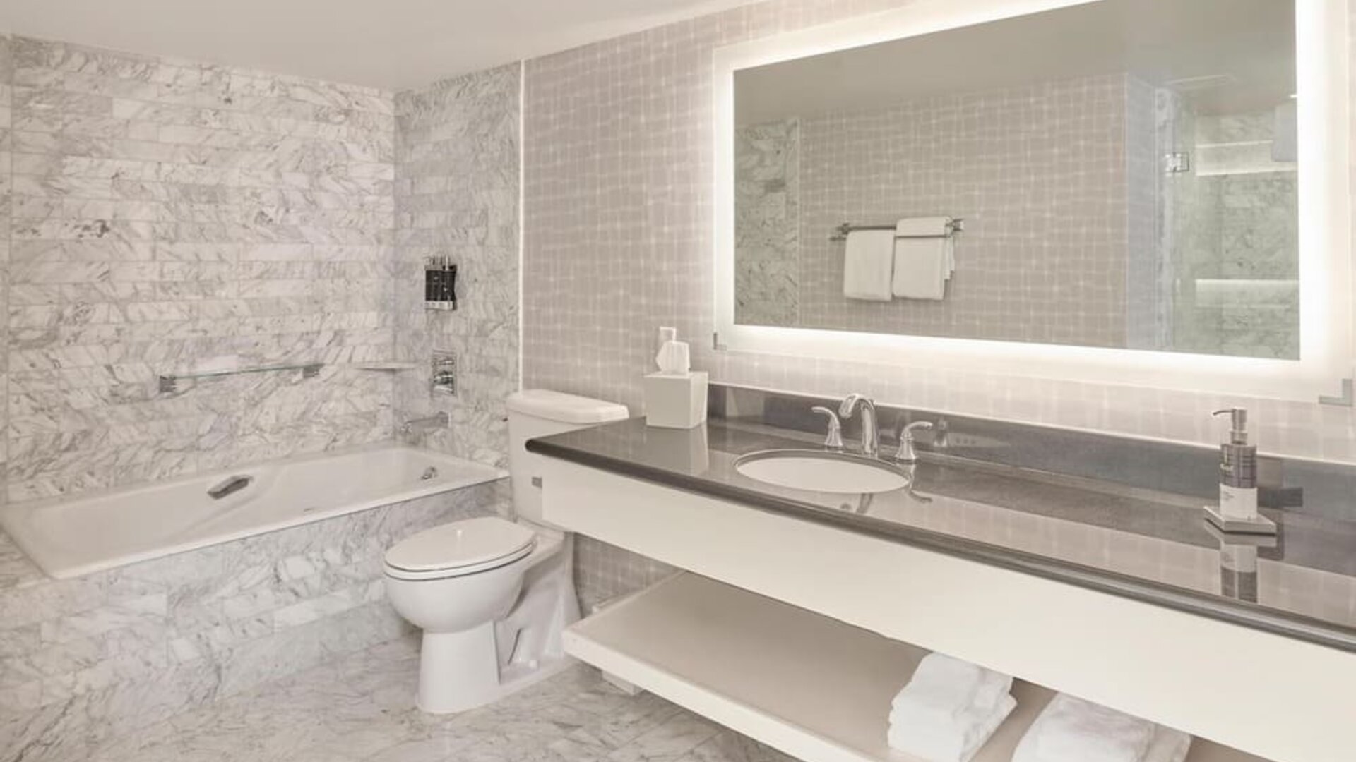 Spacious marble guest bathroom featuring a soaking tub, illuminated vanity, premium bath amenities, and modern finishes at Hyatt Centric Delfina Santa Monica.
