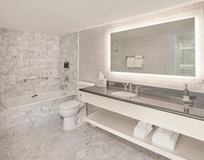 Spacious marble guest bathroom featuring a soaking tub, illuminated vanity, premium bath amenities, and modern finishes at Hyatt Centric Delfina Santa Monica.
