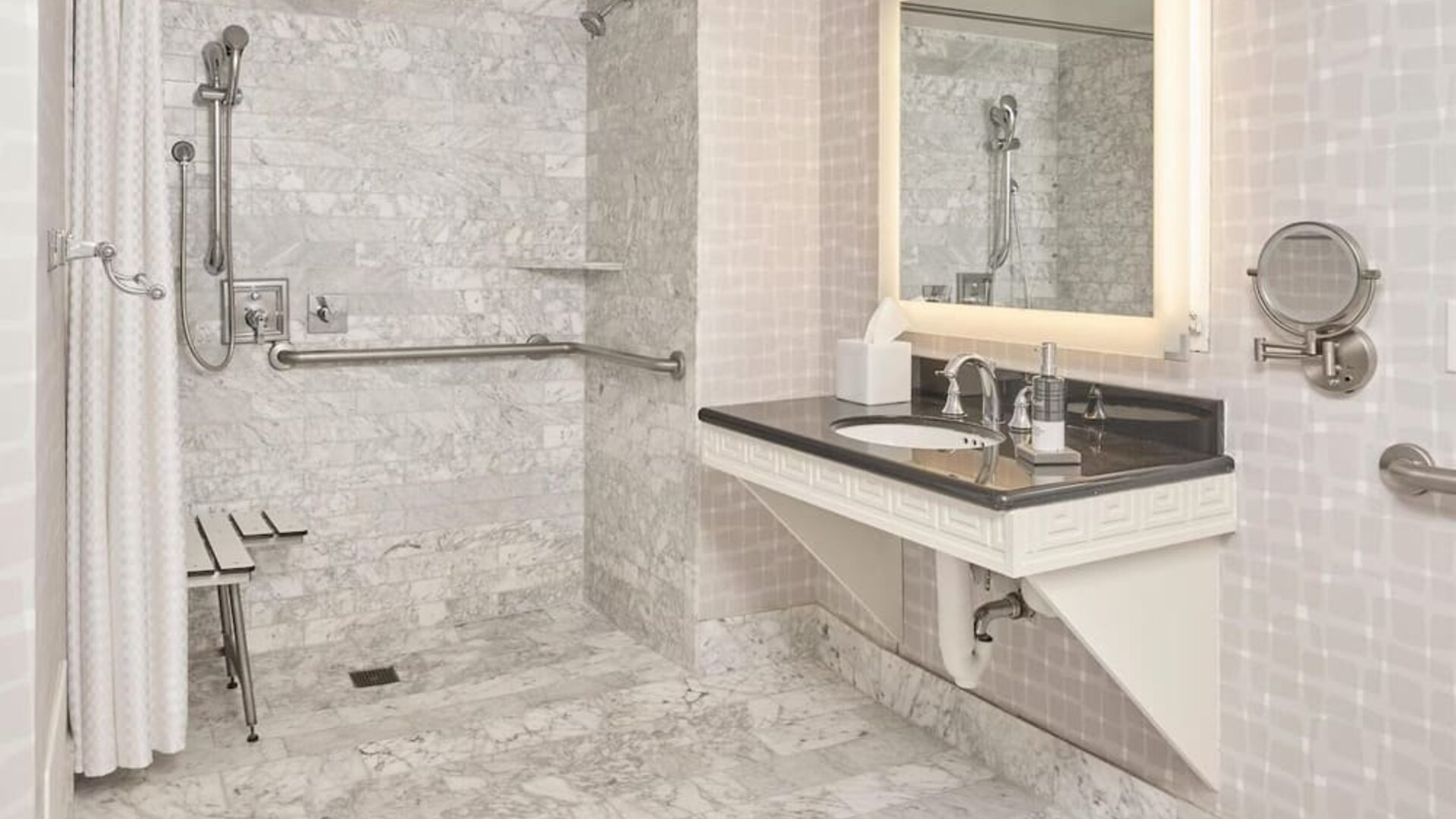 Accessible marble bathroom with roll-in shower, grab bars, illuminated vanity, and spacious design at Hyatt Centric Delfina Santa Monica.