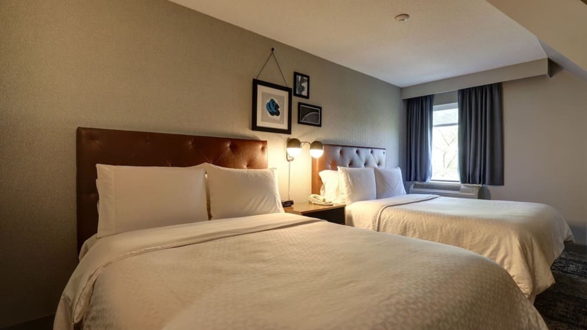 Spacious guest room with two queen beds, comfortable furnishings, and modern décor at Four Points by Sheraton St. Catharines Niagara Suites.