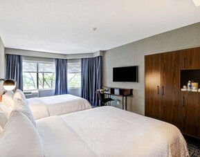 Spacious guest room featuring two plush beds, a large flat-screen TV, and modern furnishings at Four Points by Sheraton St. Catharines Niagara Suites.