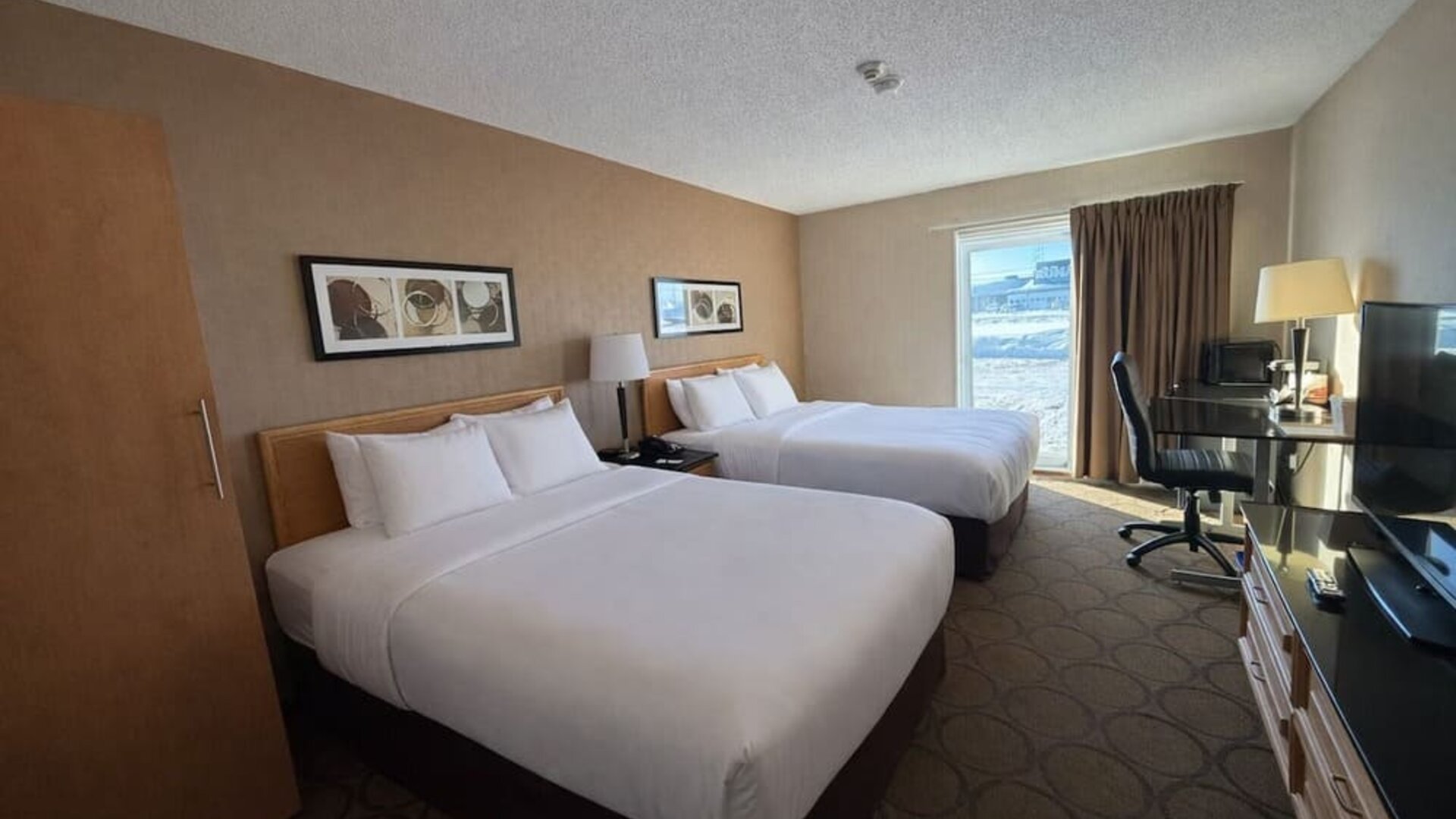 Double queen guest room with two comfortable beds, dedicated workspace, flat-screen TV, and large window at Comfort Inn Baie-Comeau.