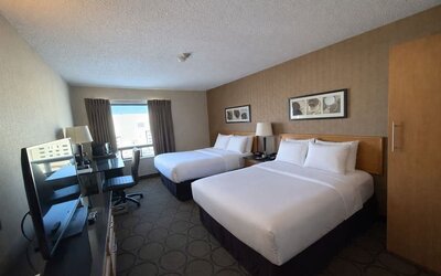 Double queen guest room offering two plush beds, workspace, flat-screen TV, and plenty of natural light at Comfort Inn Baie-Comeau.