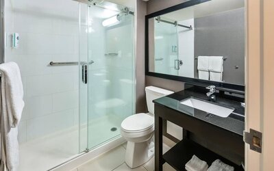 Modern guest bathroom with a glass walk-in shower, granite vanity, fresh towels, and complimentary toiletries at Comfort Inn Sudbury Regent Street.
