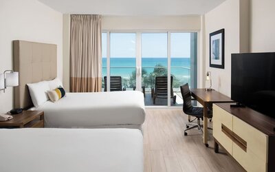 Oceanfront guest room with two beds, workspace, and private balcony at Sherry Frontenac Oceanfront Hotel.