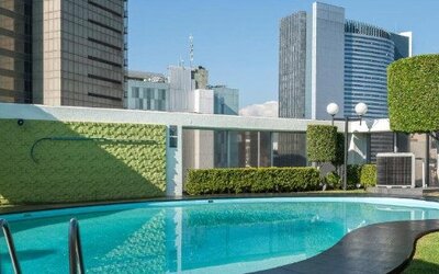 Outdoor swimming pool surrounded by landscaped greenery with high-rise city buildings beyond at Hotel Casa Blanca.