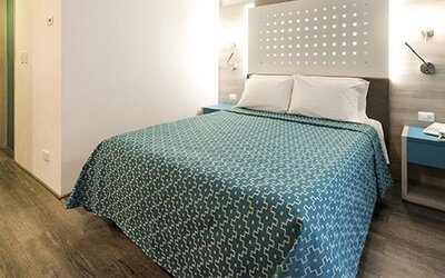 Guest room with a queen bed, illuminated headboard, bedside table and wood-look flooring at Hotel Casa Blanca.