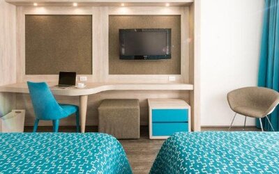 Guest room with two beds, workspace, wall-mounted TV and blue accent furnishings at Hotel Casa Blanca.