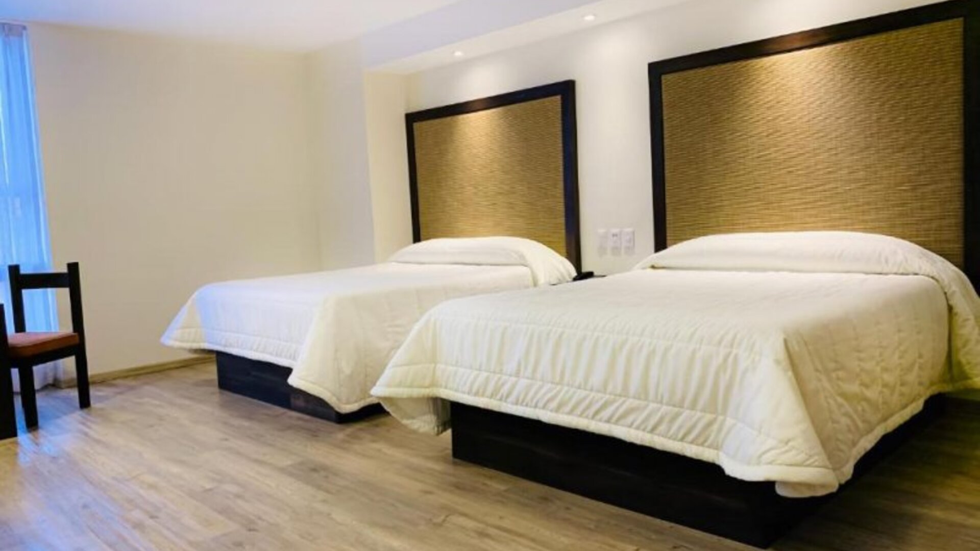 Guest room with two double beds, padded headboards and wood-look flooring at Hotel Lepanto.