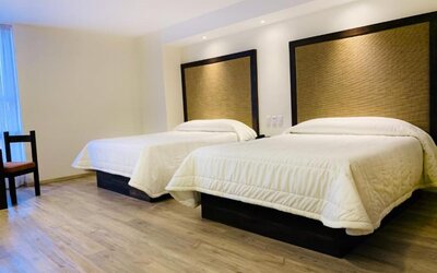 Guest room with two double beds, padded headboards and wood-look flooring at Hotel Lepanto.