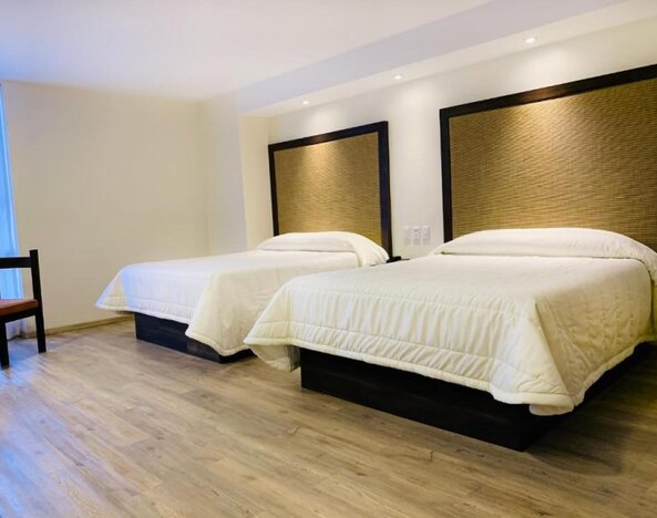 Guest room with two double beds, padded headboards and wood-look flooring at Hotel Lepanto.