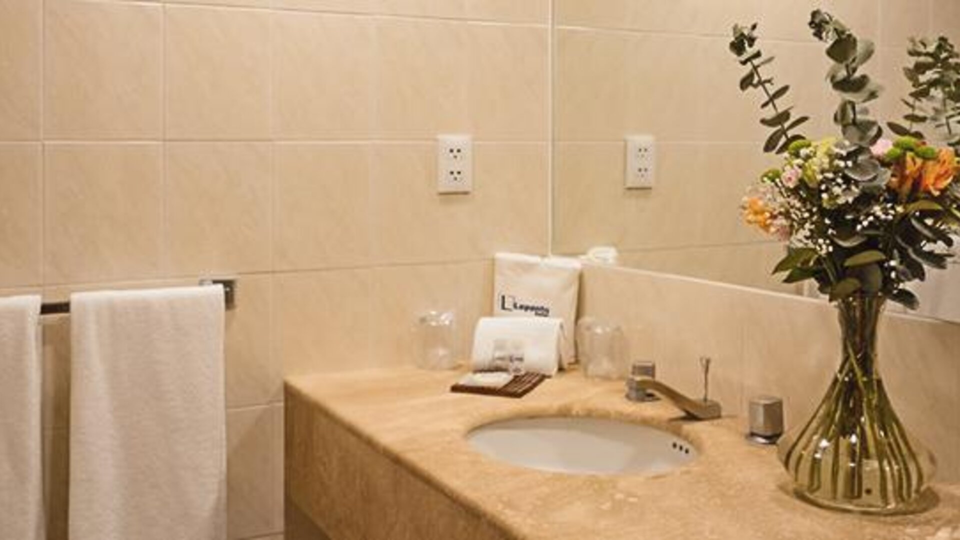 Bathroom vanity with marble countertop, fresh flowers, toiletries and neatly folded towels at Hotel Lepanto.